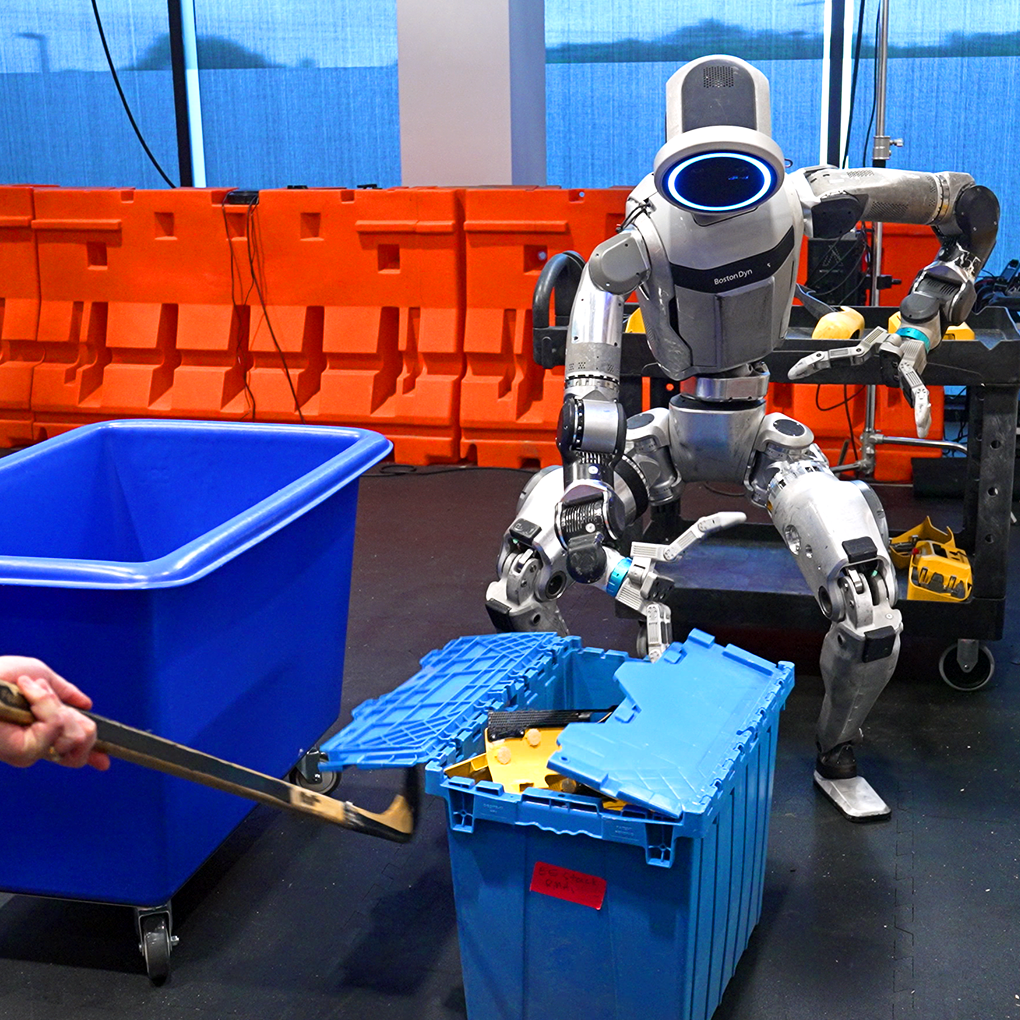 The Atlas robot leans down to open a storage bin, while an engineer closes the other side