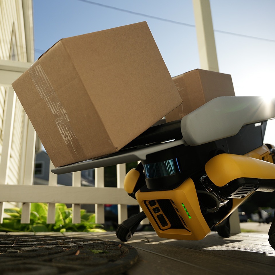 Spot robot leans down to gently place a package onto the door mat of a suburban home